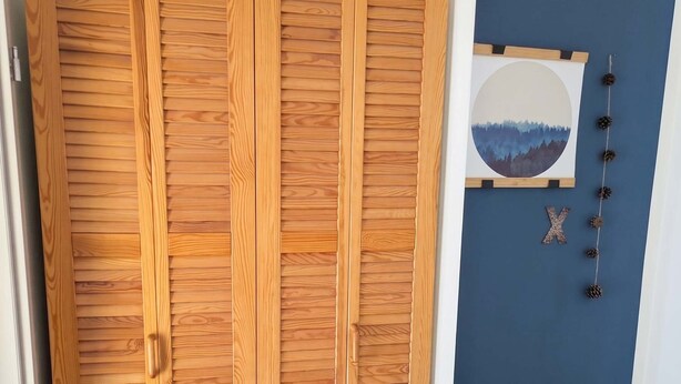 Ein Schlafzimmer mit einem Holzschrank, einem Bett mit weißer Bettwäsche, einer blauen Wand und einem gerahmten Bild.