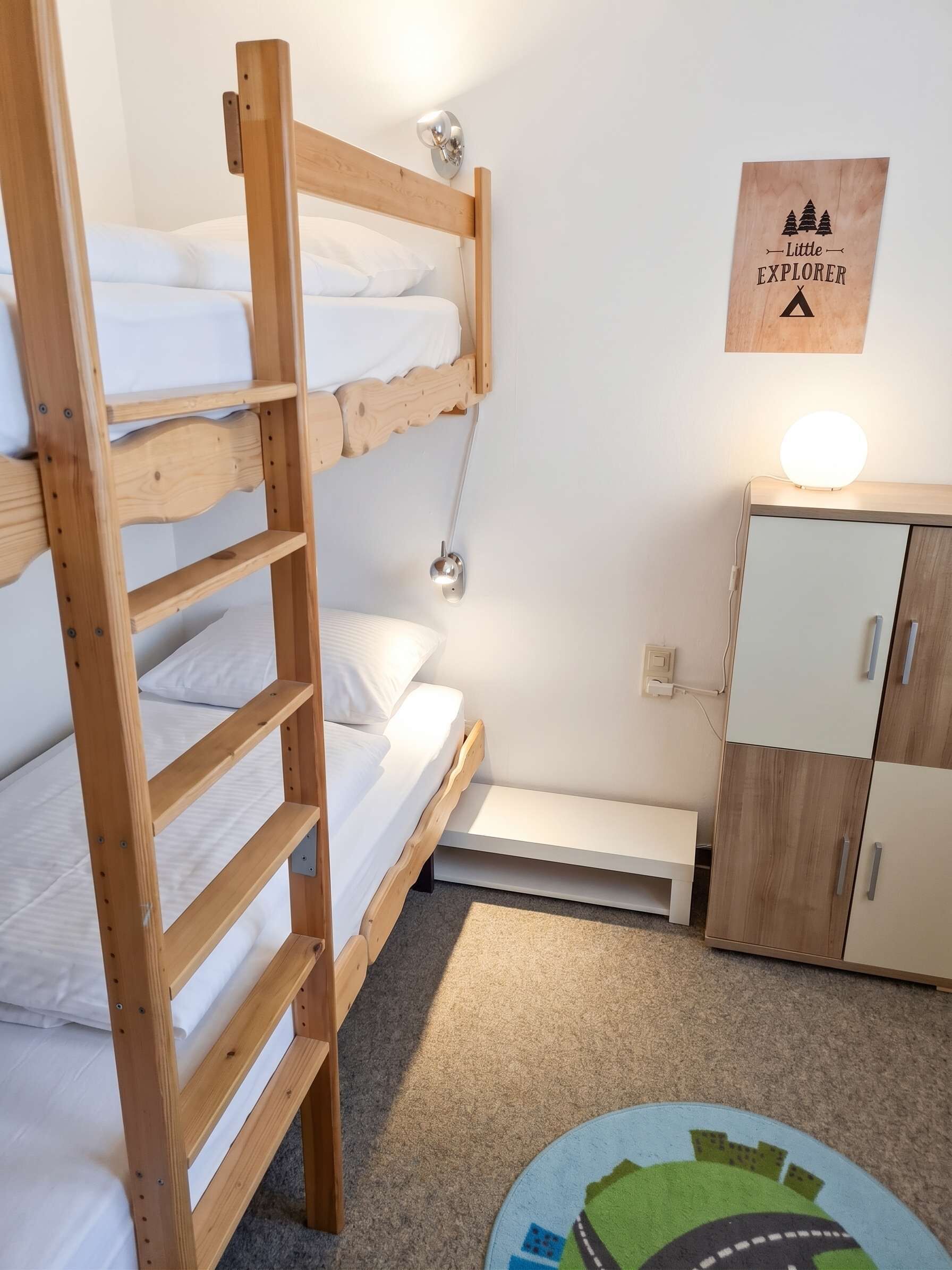 Habitación con literas, un escritorio, una lámpara, un armario y una decoración en la pared.