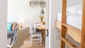 Ein Zimmer mit einem Etagenbett, einem Esstisch mit Stühlen, einer Lampe und einem Regal mit Gegenständen.