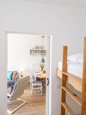 A room with a bunk bed, a dining table with chairs, a lamp, and a shelf with items. - FeWo Tannenrauschen im Ferienpark Hahnenklee (Goslar)