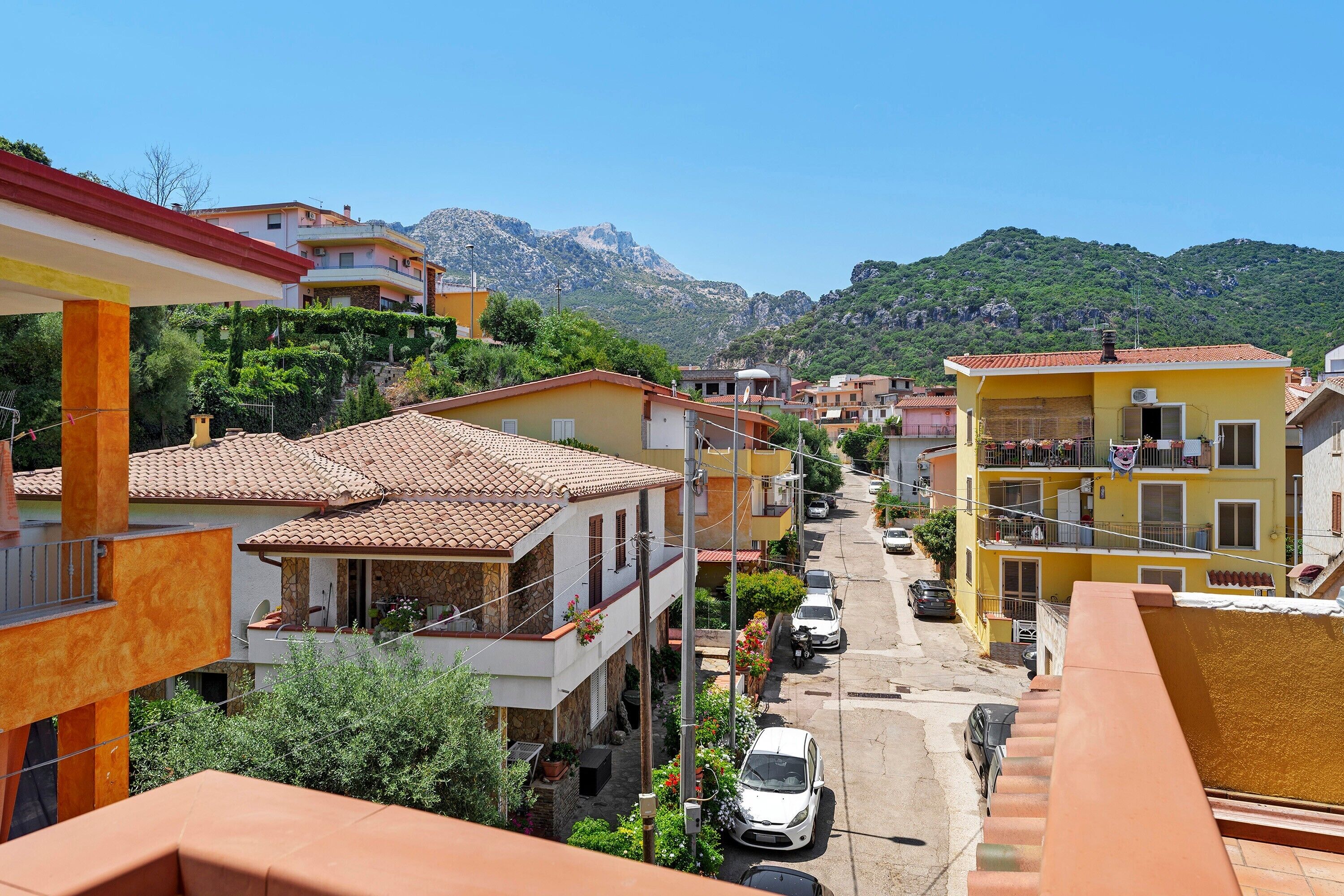A narrow street lined with colorful buildings, a parked car, and a mountain in the background.