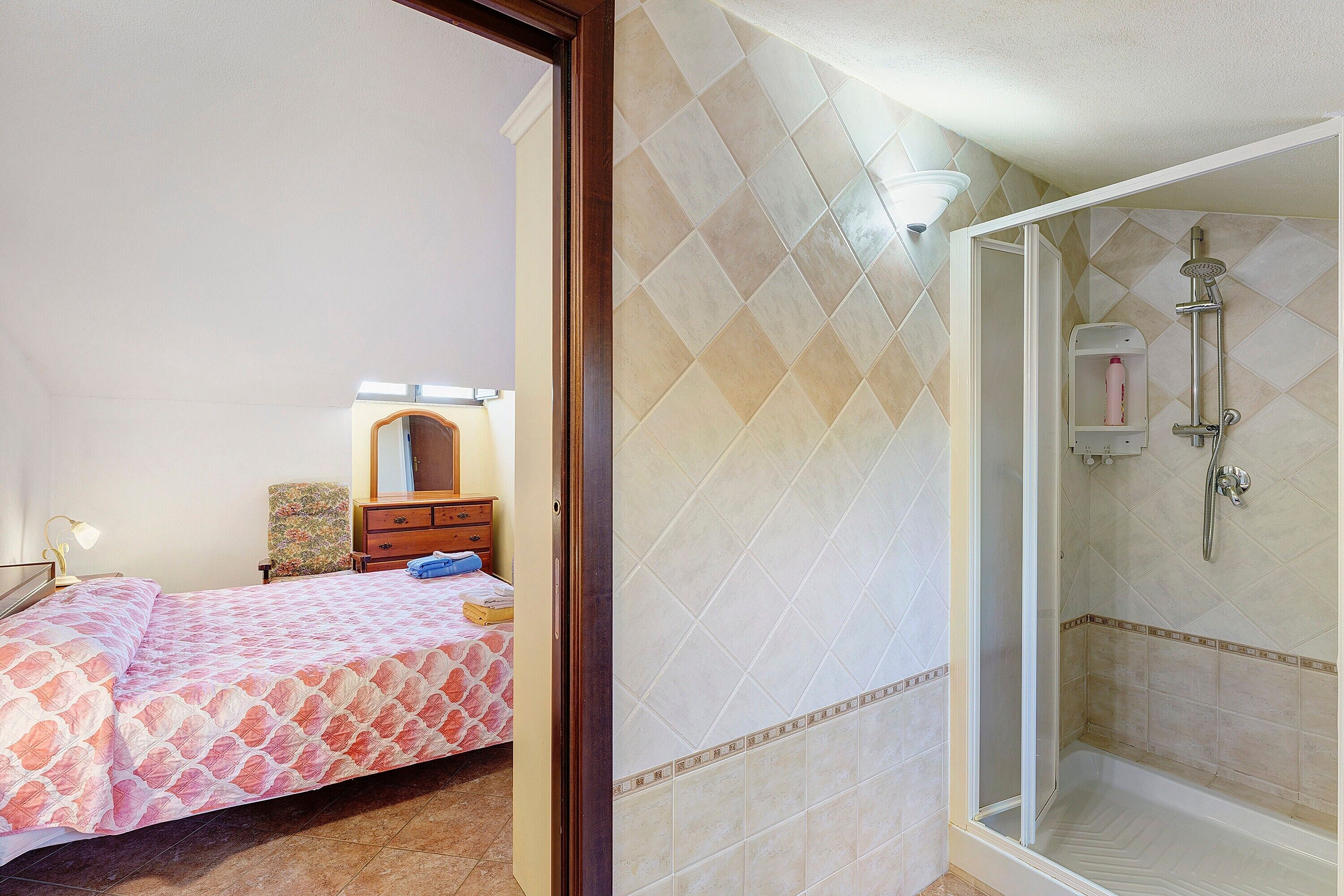 A bedroom with a bed, a dresser, a chair, and a shower area with a glass door.