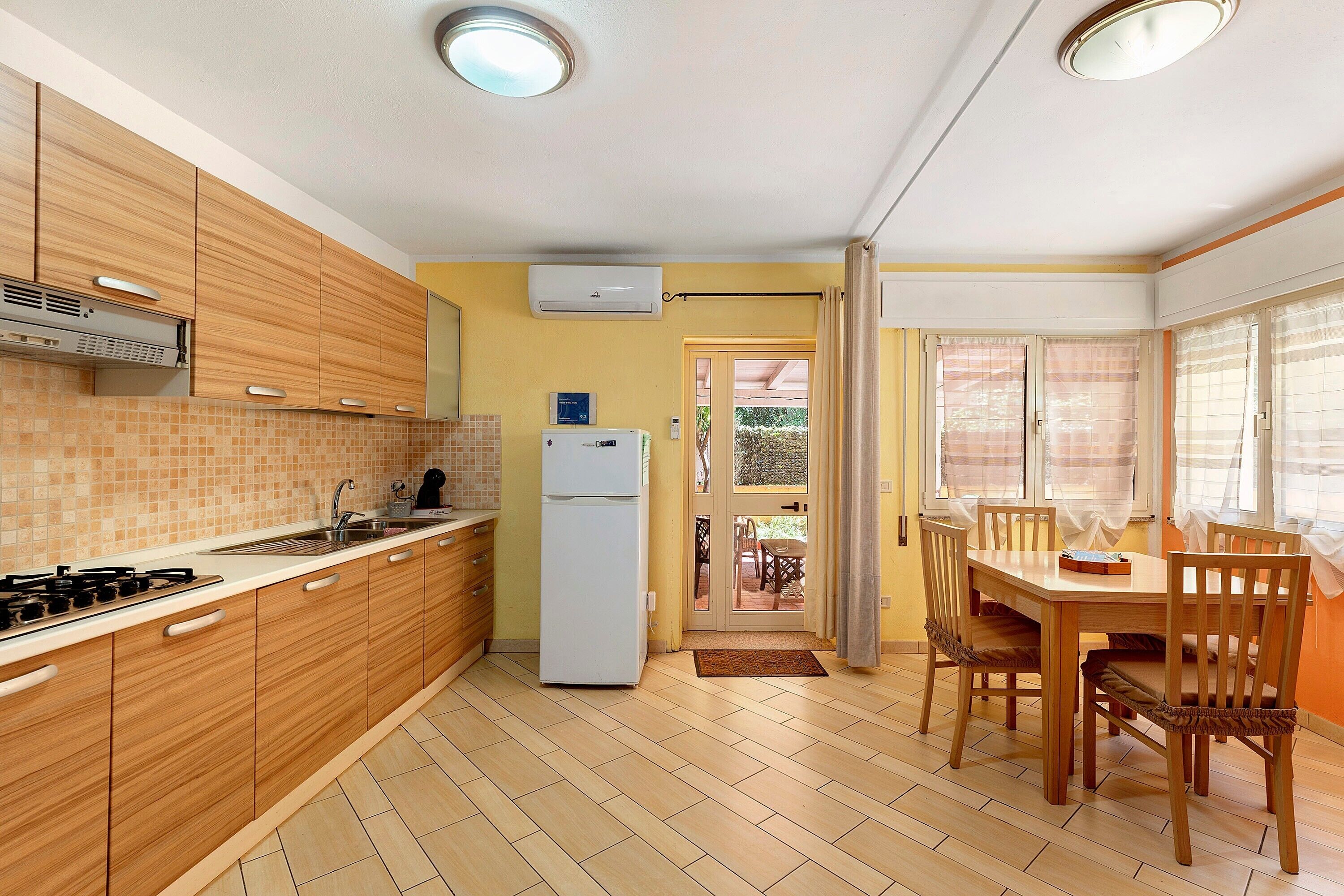 A kitchen with wooden cabinets, a refrigerator, a sink, and a dining area with a table and chairs.