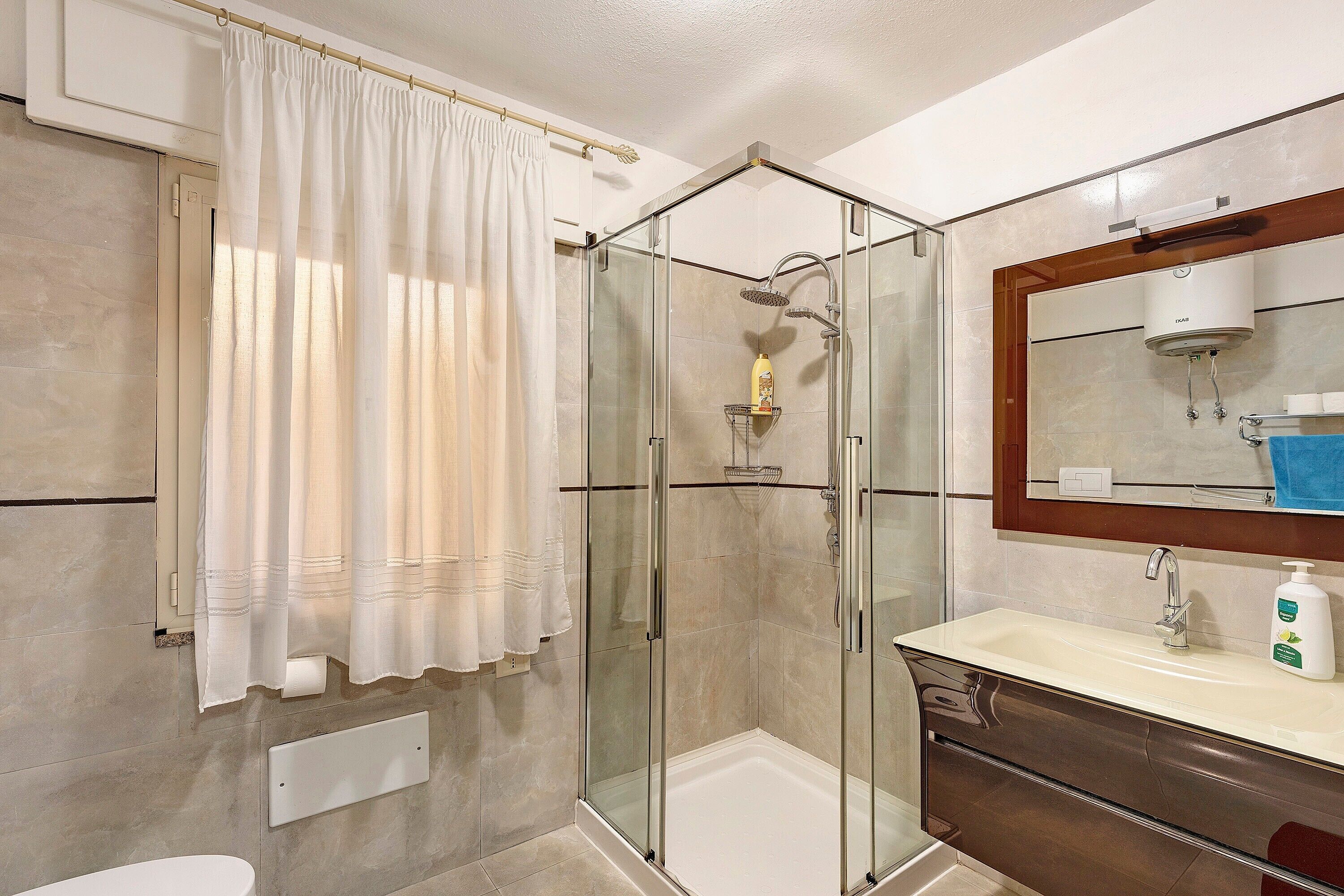 A bathroom with a glass-enclosed shower, a white sink, a mirror, and a towel rack.