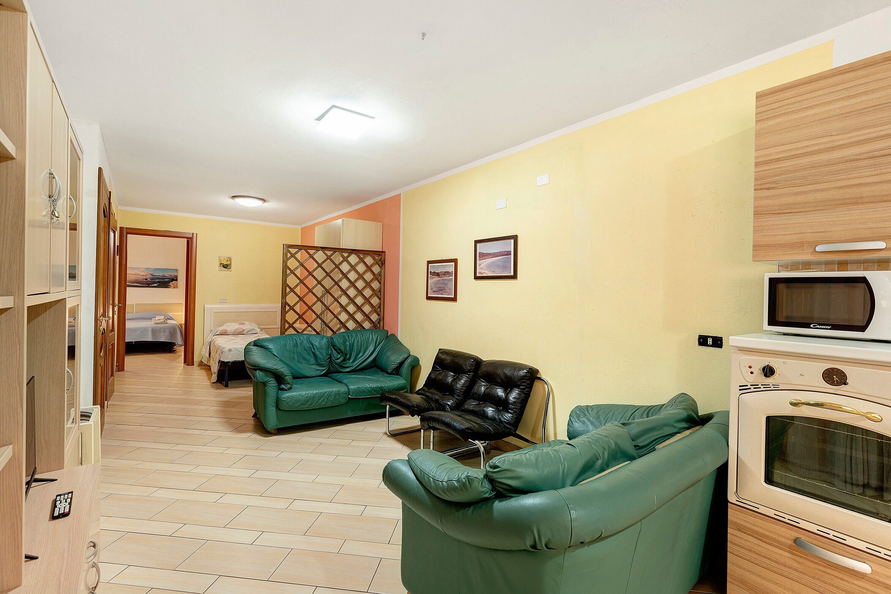 Ein Wohnzimmer mit grünen Sofas, einem schwarzen Ledersessel, einer Mikrowelle und einem Holzkasten.