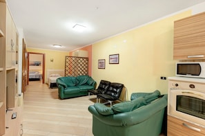 A living room with green sofas, a black leather chair, a microwave, and a wooden cabinet. - Apartment 'Casa 1 Camera Da Letto Piano Terra' with Private Terrace, Wi-Fi and Air Conditioning (Siniscola)