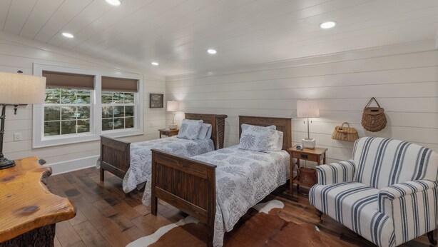 A room with two wooden beds, a wooden table, a striped armchair, and a window with blinds. - Highlands Hideaway | Close to Town, Pet Friendly, Custom Firepit (Highlands)