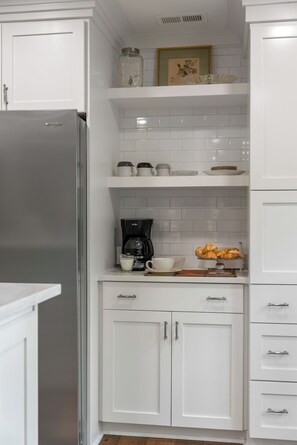 A kitchen with white cabinetry, a stainless steel refrigerator, a coffee maker, and a bowl of croissants on the counter. - Highlands Hideaway | Close to Town, Pet Friendly, Custom Firepit (Highlands)