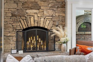 A stone fireplace with a metal screen, candles, and a vase with white flowers. - Highlands Hideaway | Close to Town, Pet Friendly, Custom Firepit (Highlands)