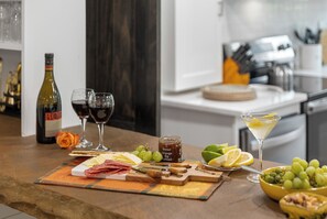 A well-lit kitchen area with a wooden countertop displaying a variety of food items and drinks, including a bottle of wine, glasses, and a martini glass. - Highlands Hideaway | Close to Town, Pet Friendly, Custom Firepit (Highlands)
