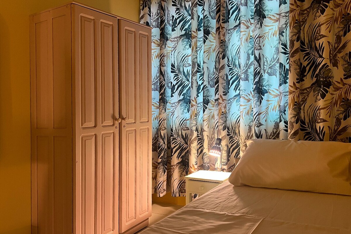 A bedroom with a bed, a wardrobe, and curtains with a leaf pattern.