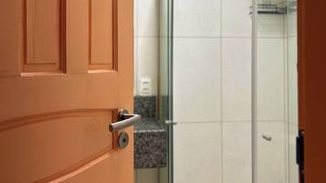 A bathroom with a wooden door, a glass shower enclosure, and a white towel hanging on the shower door handle.