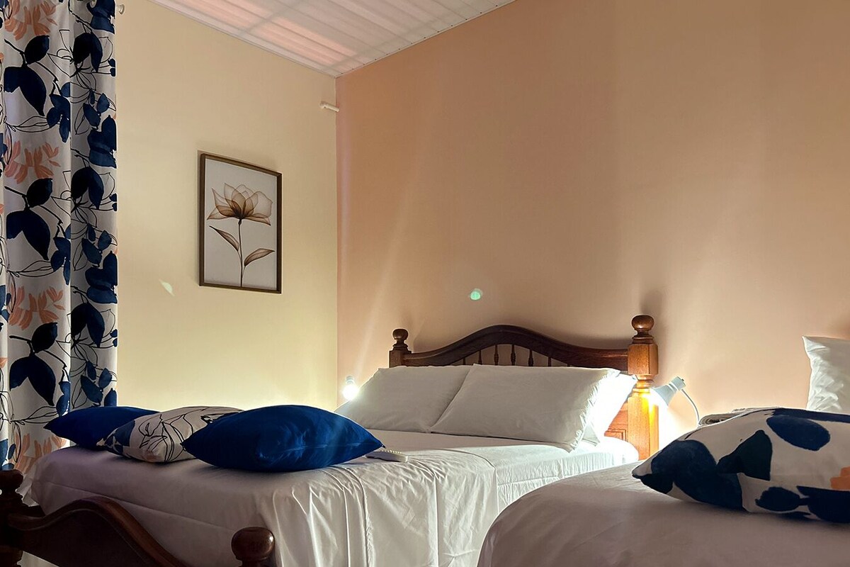 A bedroom with two beds, a wooden headboard, a framed picture on the wall, and a curtain with a leaf pattern.
