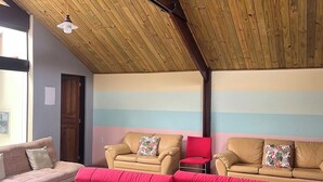 Et værelse med skråvægge, en pink sofa, beige lænestole og en rød stol.
