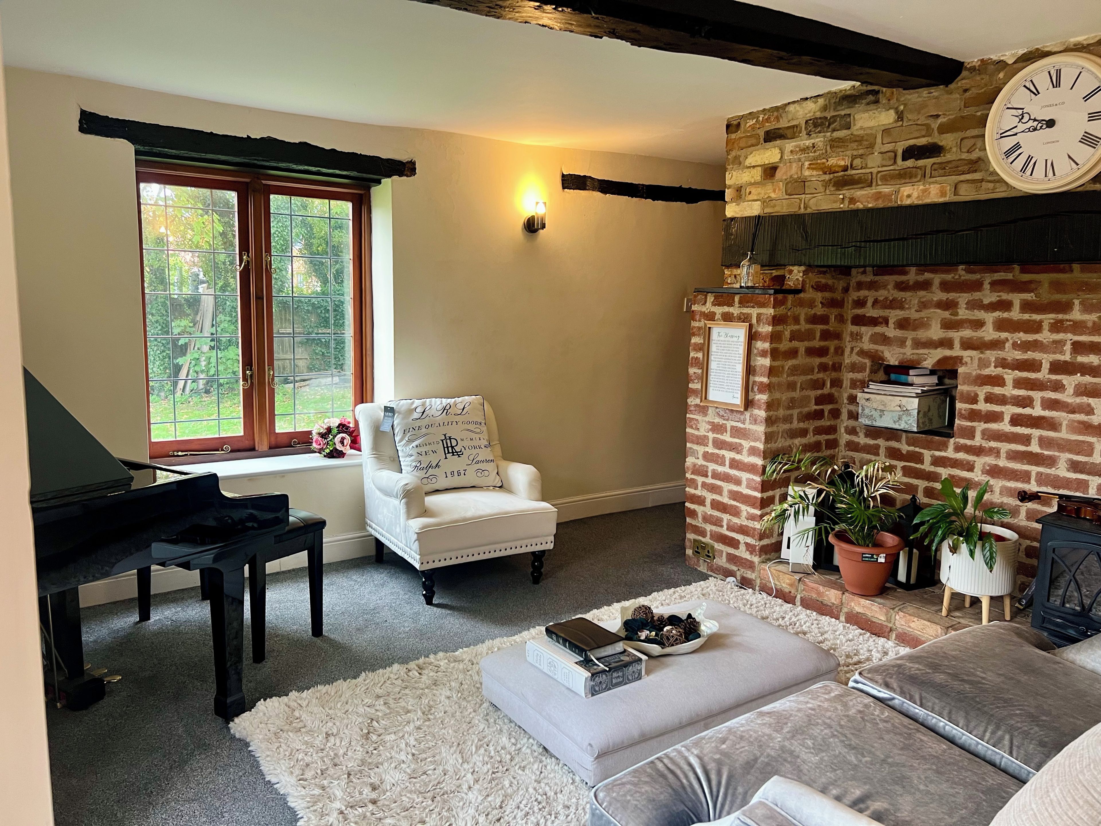 A cozy living room with a piano, a white armchair, a fireplace, and a clock on the wall.