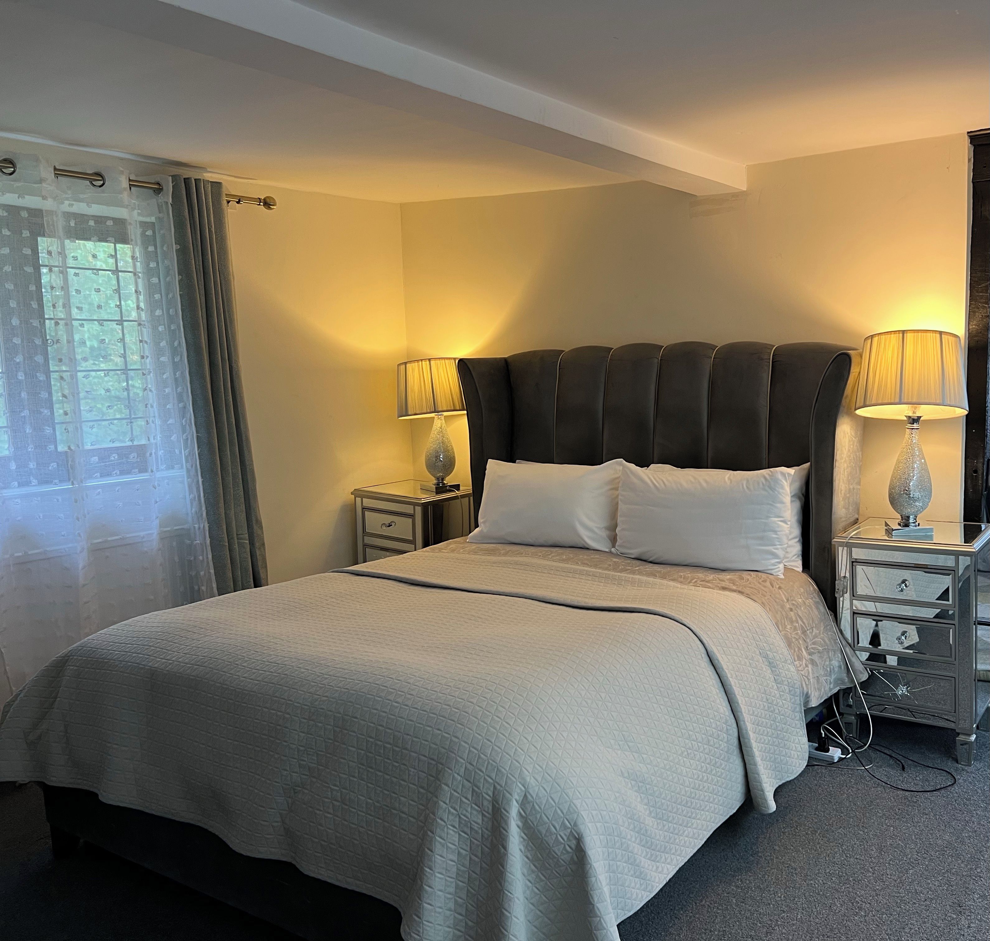 A hotel room with a large bed, two bedside tables, a window with curtains, and a lamp on each table.