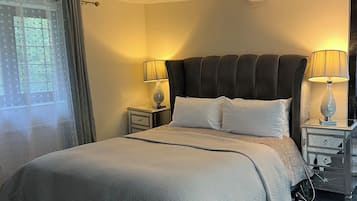 A hotel room with a large bed, two bedside tables, a window with curtains, and a lamp on each table.