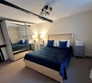 Ein Hotelzimmer mit einem großen Bett, einem Nachttisch, einem Spiegel und einem Deckenventilator.