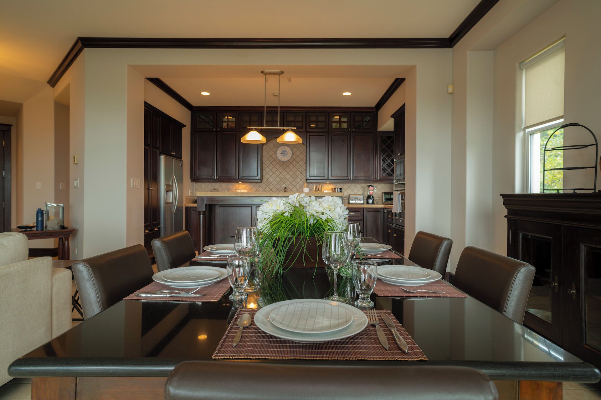A dining area with a glass table set for six, surrounded by dark wooden chairs.