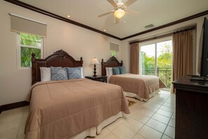 A hotel room with two beds, a ceiling fan, a TV, and a balcony with curtains. - Vista Bahia 2C 3 bdr Ocean View in Los Suenos (Herradura)