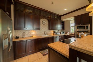 A kitchen with dark wood cabinets, a stainless steel refrigerator, a microwave, and a dishwasher. - Vista Bahia 2C 3 bdr Ocean View in Los Suenos (Herradura)