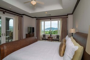 Ein Hotelzimmer mit einem großen Bett, einem Fernseher, einem Balkon mit Stühlen und Blick auf die Landschaft.