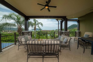 A covered outdoor seating area with a view of a green landscape and hills. - Vista Bahia 2C 3 bdr Ocean View in Los Suenos (Herradura)