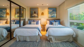 Ett hotellrum med två sängar, en takfläkt, ett stort fönster med utsikt över grönområden och konstverk på väggarna.