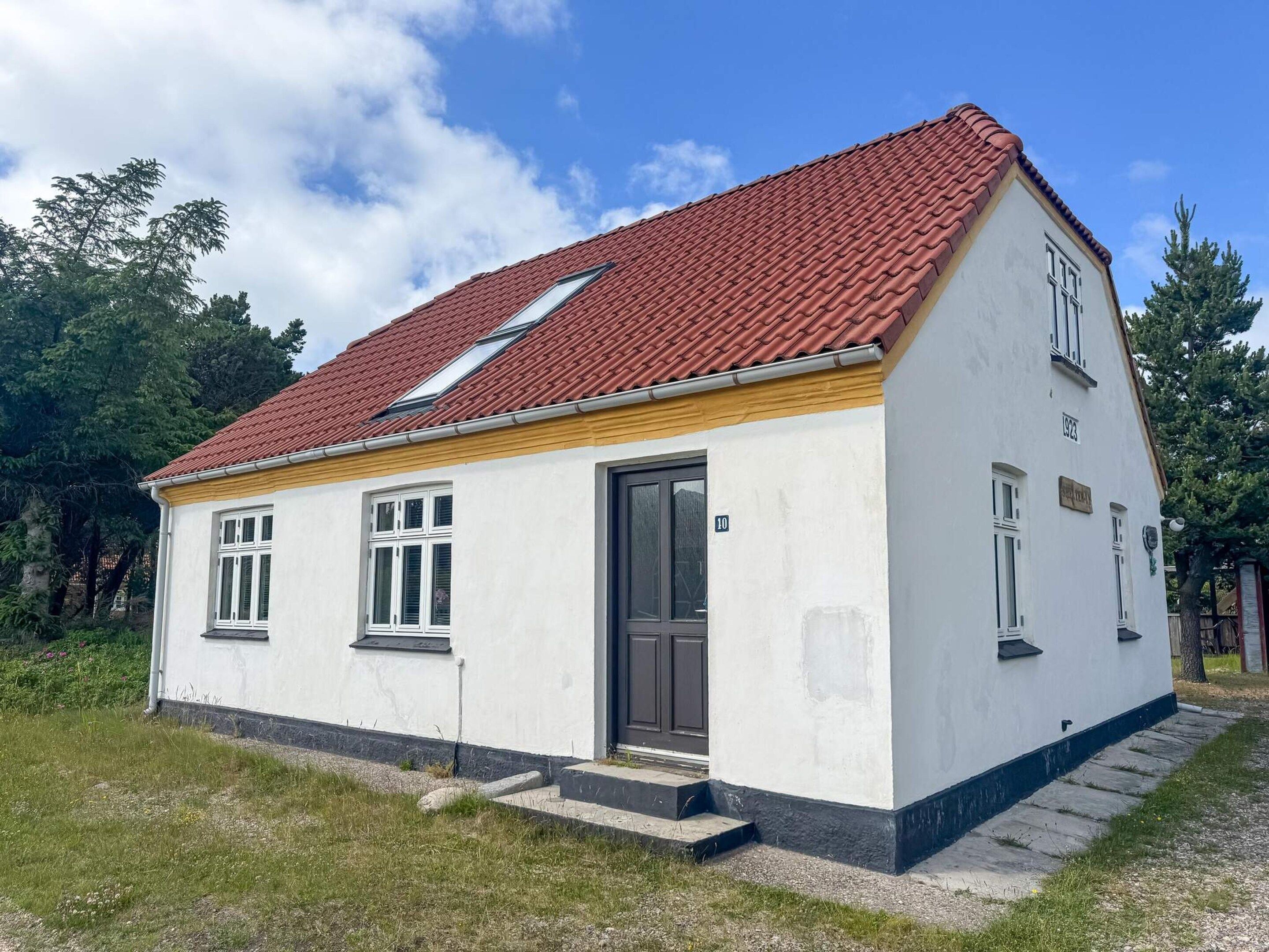 A single-story building with a red-tiled roof, a black door, and a small porch.