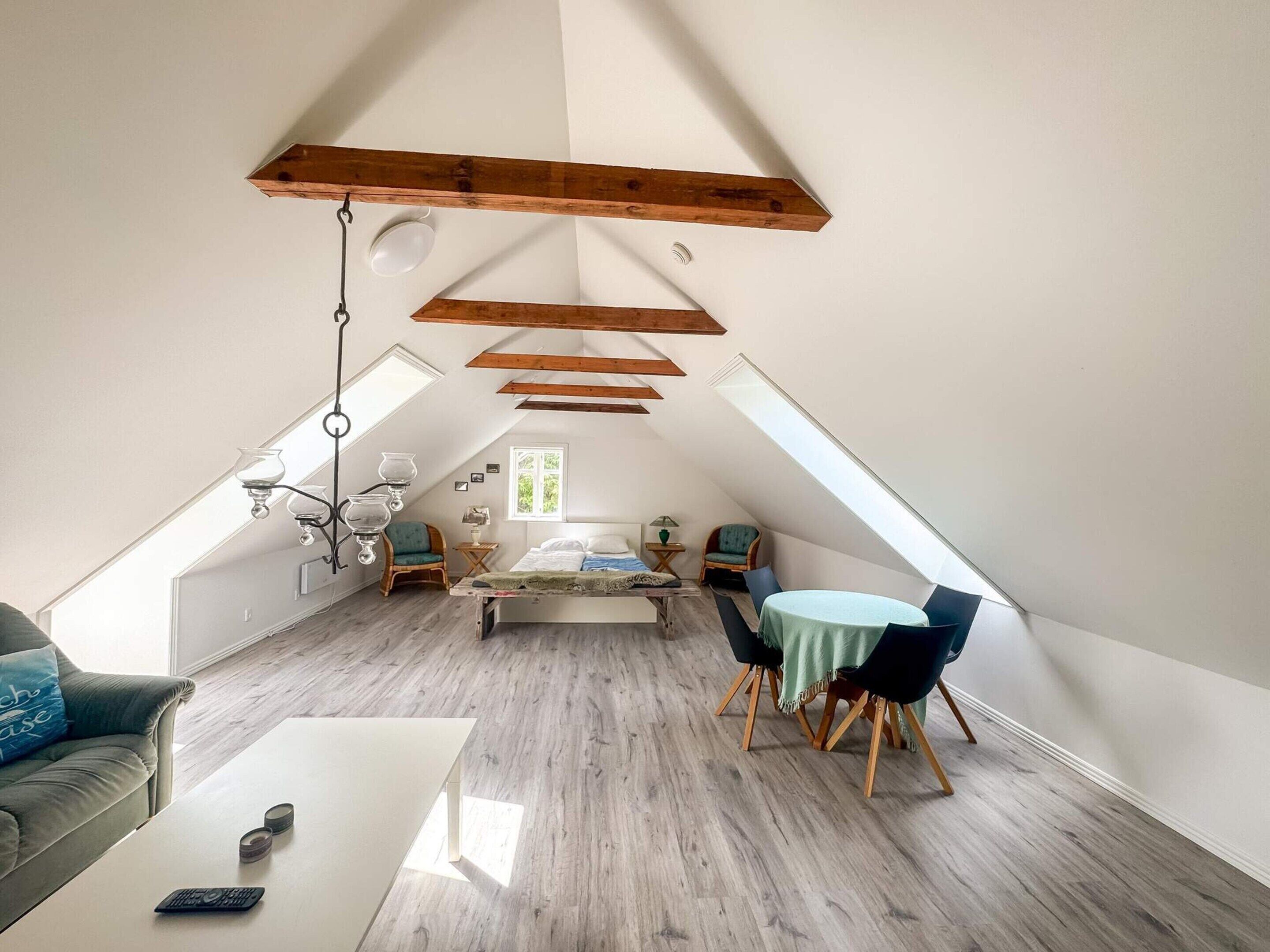 Une pièce de style loft avec un plafond en pente, des poutres en bois, un lit, une table à manger et un canapé.