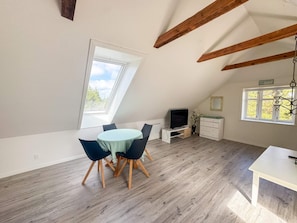 A room with a sloped ceiling, a dining table with chairs, a TV stand, and a window with a view of trees. - 6 Person Holiday Home in Bedsted Thy (Bedsted)