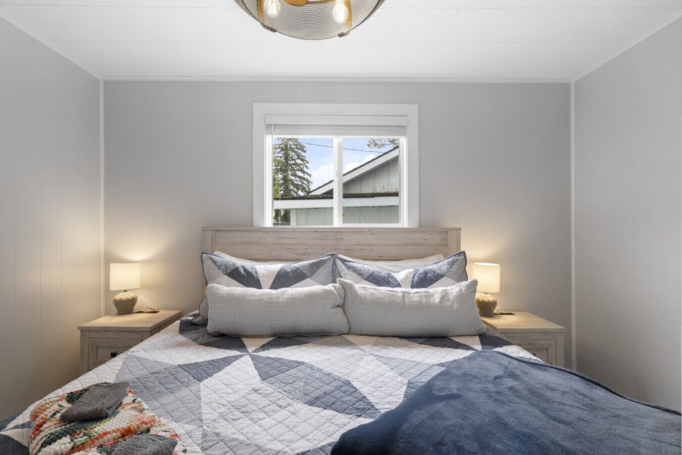 Une chambre à coucher avec un lit, deux lampes de chevet, une fenêtre et une vue sur un immeuble.