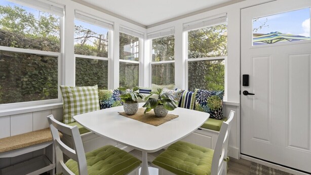 A sunlit room with a white table, green cushioned seating, and large windows.