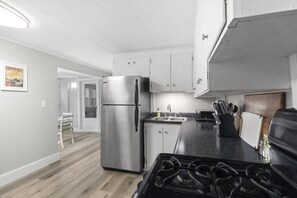 A modern kitchen with a stainless steel refrigerator, a gas stove, and white cabinetry.