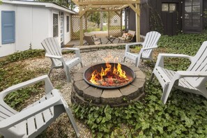 A circular fire pit with chairs around it, set on a gravel surface with ivy.