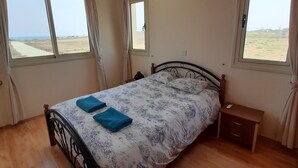 A bedroom with a bed, two windows, a bedside table, and a hanging light fixture. - Beautiful Sea Views Private Pool 3 Bed Beach Villa (Perivolia)