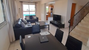 A modern living room with a sofa, dining table, and TV. - Beautiful Sea Views Private Pool 3 Bed Beach Villa (Perivolia)