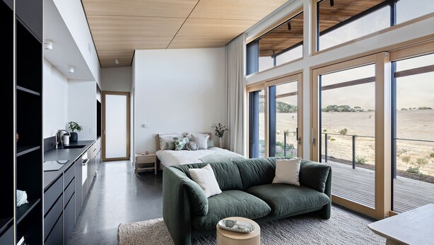 A modern bedroom with a large window, a sofa, a bedside table, and a TV. - Studio on Forktree – Modern Coastal Retreat (Carrickalinga)