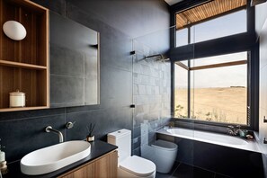 A modern bathroom with a large window, a bathtub, a sink, and a toilet.