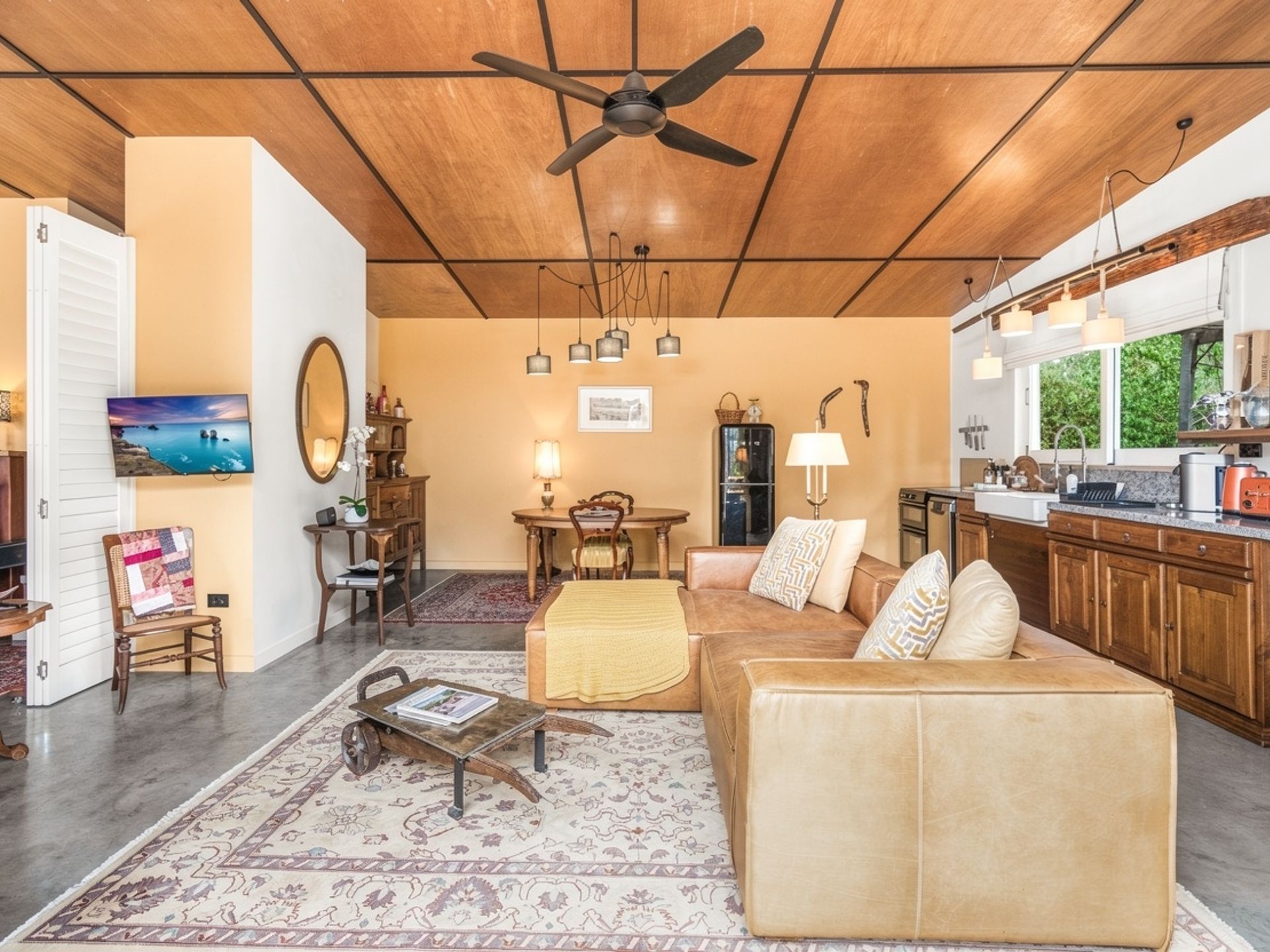 Uma sala de estar ampla com ventilador de teto, área de jantar com mesa e cadeiras e cozinha equipada com eletrodomésticos modernos.