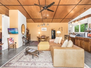 Uma sala de estar ampla com ventilador de teto, área de jantar com mesa e cadeiras e cozinha equipada com eletrodomésticos modernos.