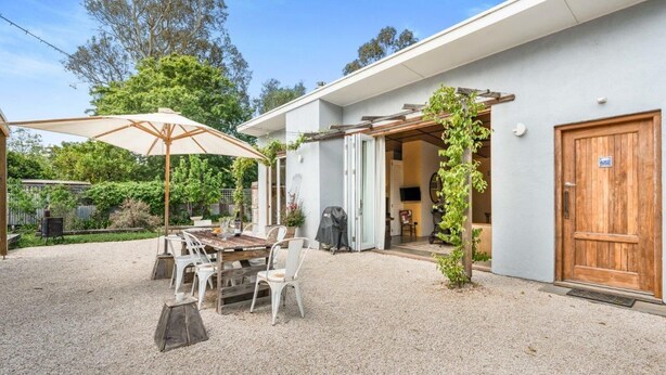 Um pátio com mesa e cadeiras, uma porta de madeira e uma área coberta com guarda-sol.