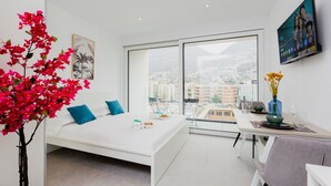Ein modernes Schlafzimmer mit Bett, Essbereich und großem Fenster mit Blick auf die Stadt.