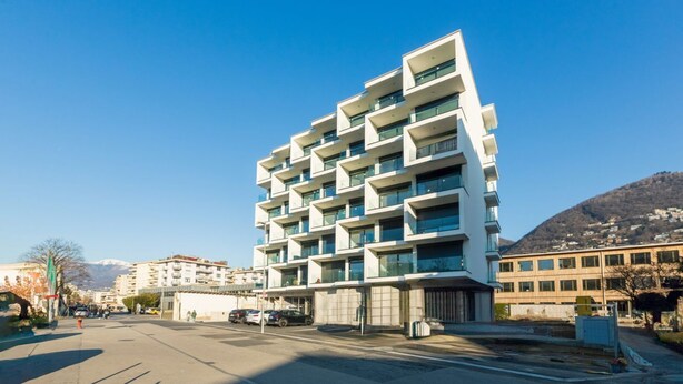 Ein mehrstöckiges Gebäude mit Balkonen und einer glatten Fassade, bewölkter Himmel.