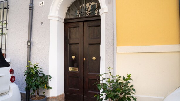A double wooden door with a small window above it, a white wall with a number '49' sign, and two potted plants on the ground. - A comfortable 34 square-meter studio apartment that sleeps up to three people, located on the ground floor of a renovated building.The property enjoys a strategic location just steps from Ravenna's historic center, in a quiet residential area well-served (Ravenna)