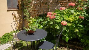 A round metal table with two chairs, a potted plant, and a brick wall with flowering plants. - A comfortable 34 square-meter studio apartment that sleeps up to three people, located on the ground floor of a renovated building.The property enjoys a strategic location just steps from Ravenna's historic center, in a quiet residential area well-served (Ravenna)
