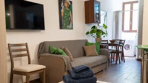 A living room with a sofa, a television, a painting, a potted plant, and a dining area with chairs and a table. - A comfortable 34 square-meter studio apartment that sleeps up to three people, located on the ground floor of a renovated building.The property enjoys a strategic location just steps from Ravenna's historic center, in a quiet residential area well-served (Ravenna)