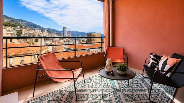 Un balcone con vista sulla città, due sedie, un tavolino con una pianta e un tappeto decorato.