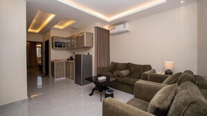 Una sala de estar moderna con un conjunto de sofás, una mesita de centro y una cocina con armarios y electrodomésticos.