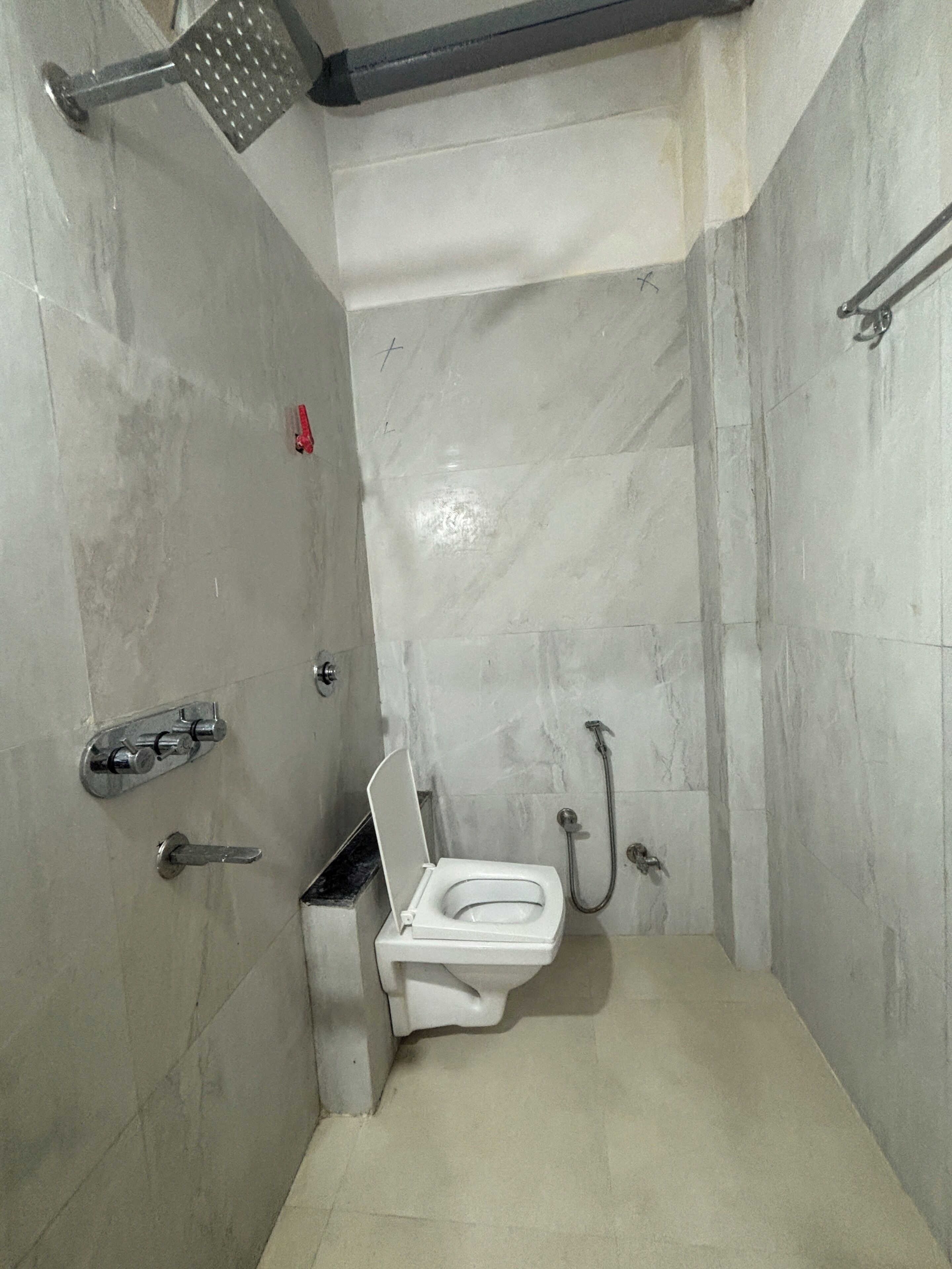 A small, tiled bathroom with a toilet, a shower, and a handrail.
